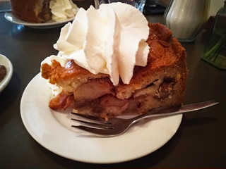 typical Dutch dish. apple pie, the best cake in all of Amsterdam. apple pie accompanied by a lot of whipped cream and placed on a white plate together with the cutlery