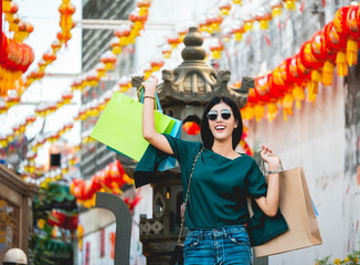 Asian women are addicted to shopping or shopaholic shopping in the china town with colorful paper shopping bags during the discount season with copy space and blur city background, Soft tone.