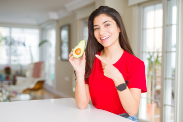 Young woman eating healthy avocado very happy pointing with hand and finger