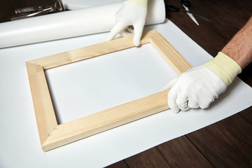 Canvas, wooden stretcher bar and male hand in white protect gloves