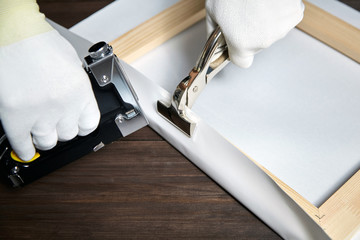 Canvas stretching. Wooden stretcher bar, staple gun, canvas pliers, male hand in white protect...
