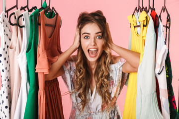 Photo of emotional woman in dress standing inside wardrobe rack full of clothes