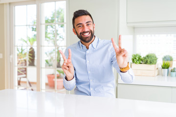 Handsome hispanic business man smiling looking to the camera showing fingers doing victory sign. Number two.