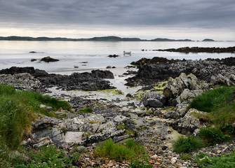 Fototapeta na wymiar Sand beach and rocky shore and clouds on Isle of Iona with boat on Sound of Iona Inner Hebrides Scotland UK