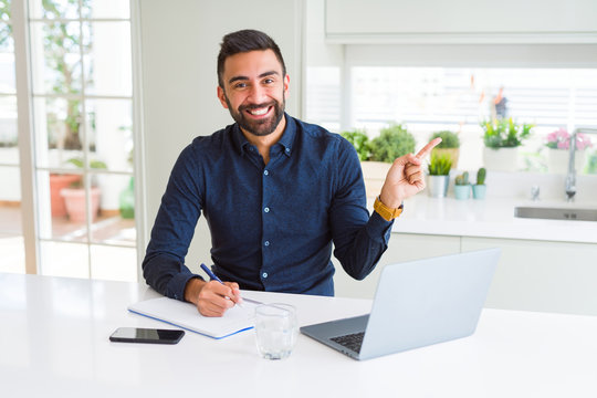 Handsome hispanic man working using computer and writing on a paper very happy pointing with hand and finger to the side