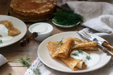 Buckwheat pancakes served with sour cream and dill on a wooden table. Rustic style.