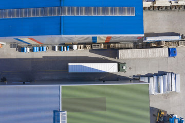 Aerial view, logistic warehouse, trucks ride near warehouse ramp.