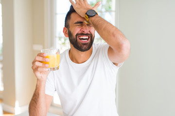 Handsome hispanic man drinking healthy orange juice stressed with hand on head, shocked with shame...