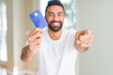 Handsome hispanic man holding credit card pointing with finger to the camera and to you, hand sign,...