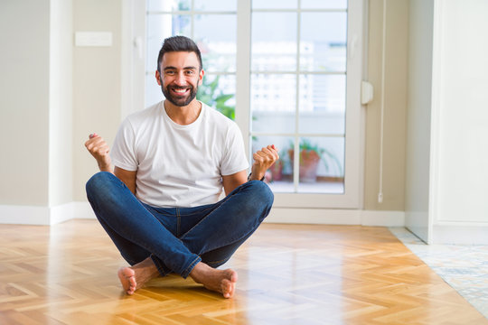 Handsome hispanic man wearing casual t-shirt sitting on the floor at home celebrating surprised and amazed for success with arms raised and open eyes. Winner concept.