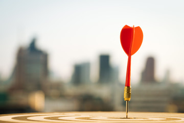 Red dart arrow hitting in the target center of dartboard with city background. Target business,...