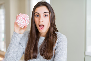 Beautiful young woman eating sugar marshmallow pink donut scared in shock with a surprise face, afraid and excited with fear expression