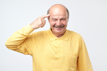 senior man smiling pointing to head with one finger, great idea or thought