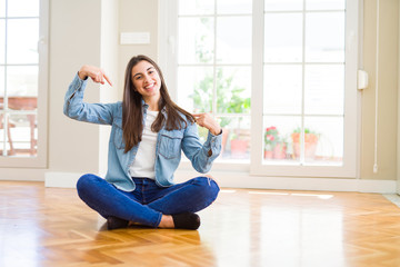 Beautiful young woman sitting on the floor at home looking confident with smile on face, pointing oneself with fingers proud and happy.