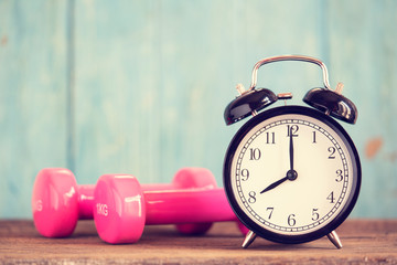 Time for exercising alarm clock and dumbbell on the table with green background, sport and workout...