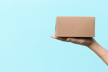 Woman hand hold the brown corrugated box on blue  wall background with copy space
