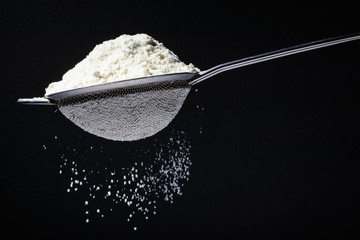 Flour is poured into a sieve, which sifts it. Dark and black background. Flour movement.