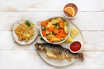 Smażona ryba z warzywami i surówką z kapusty. Apetyczna potrawa na jasnym talerzu na drewnianym...