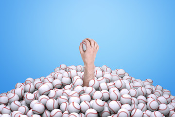 Man's hand holding a baseball, emerging from under a big pile of baseballs.