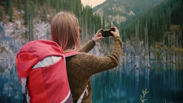 Female traveler and backpacker finally reached Freedom destination of virgin nature in green mountain pine woods trees growing from Kaindy lake and taking photo picture by smartphone or mobile phone