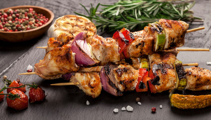 Grilled chicken skewers with spices and vegetables on black background