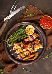 Grilled chicken skewers with spices and vegetables in a pan on dark background