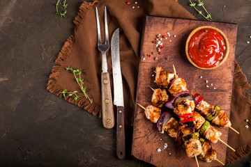 Grilled chicken skewers with spices and vegetables on cutting board and dark background