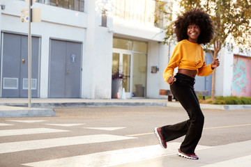 Fototapeta na wymiar Fashionable young black woman with afro hair running across the street, full length, close up