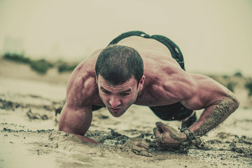 Closeup of strong athletic, muscular man crawling in wet muddy puddle in the rain in an extreme...