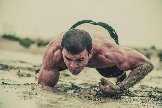 Closeup of strong athletic, muscular man crawling in wet muddy puddle in the rain in an extreme competitive sport 