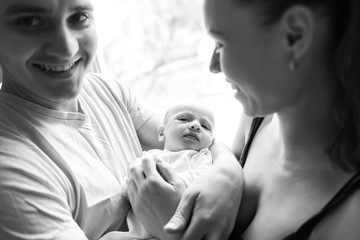 Woman and man holding on hands a newborn. On the background window. Mom, dad and baby. Portrait of young family. Happy family life. Man was born.