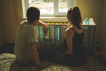 A man and a woman sitting next to the crib. Scene from family life. Future parent.