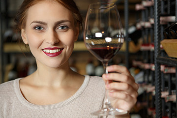 My choice. Closeup shot of an attractive smiling red lipped woman holding a glass of red wine standing in a wine cellar