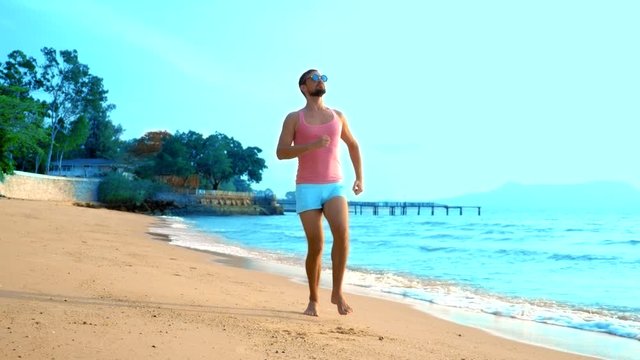 A playful handsome guy in a pink t-shirt and blue shorts joyfully runs into the sea. freak on the sea