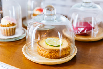 Mini Key Lime Pie topping with slice of lime in wooden plate and cover with glass cloche.