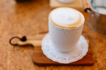Hot Latte served in ceramic cup on wooden plate. Smooth white and brown froth.