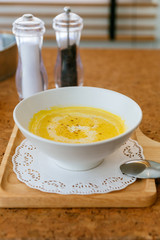 Classic Pureed Pumpkin Soup topping with Milk, Cream and Pepper. Served on wooden plate with salt, garlic and cutlery.