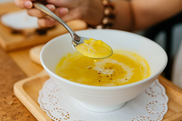 Obraz na płótnie Canvas Female Hand Scooping Classic Pureed Pumpkin Soup topping with Milk, Cream and Pepper with silver spoon.