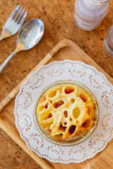 Top view of Cheese Baked Penne in glass bowl on wooden plate with salt, pepper and cutlery.
