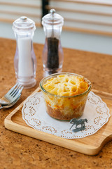 Cheese Baked Penne in glass bowl on wooden plate with salt, pepper, cutlery and miniature horse model.