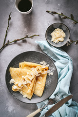 Crepes with bananas and almond slices and coffee on a dark background