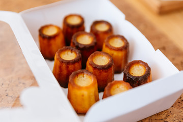 Fresh baked Canelés inside white paper box. A small French pastry flavored with rum and vanilla with a soft and tender custard center and a dark, thick caramelized crust.