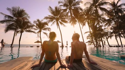 Couple relaxing at tropical beach resort and talking together at sunset, summer vacation holidays destination, scenic landscape with the sea and coconut palm trees, romantic honeymoon - Powered by Adobe