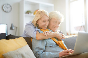 Obraz premium Portrait of happy senior woman embracing husband working with laptop in sunlight, copy space