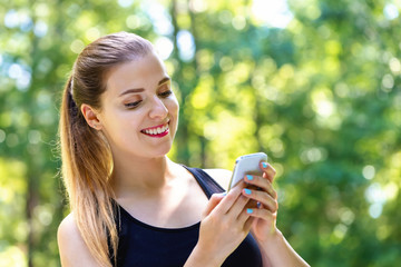Young woman using her cellphone on a bright summer day in the forest