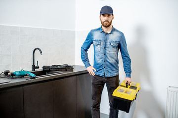 Portrait of a handsome repairman in blue shirt and cap with tool case on the kitchen