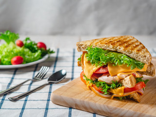 Close up of Sandwich with ham, cheese, tomatoes, lettuce, and toasted bread on the  wooden cutting board.