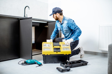 Handyman in blue shirt and cap mounting or repairing kitchen furniture in the apartment
