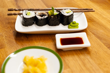 Homemade vegan Sushi rolls filled with avocado on a small plate on a wooden table with soy sauce, wasabi and ginger
