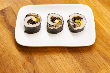Homemade vegan Sushi rolls filled with avocado on a small plate on a wooden table with soy sauce, wasabi and ginger